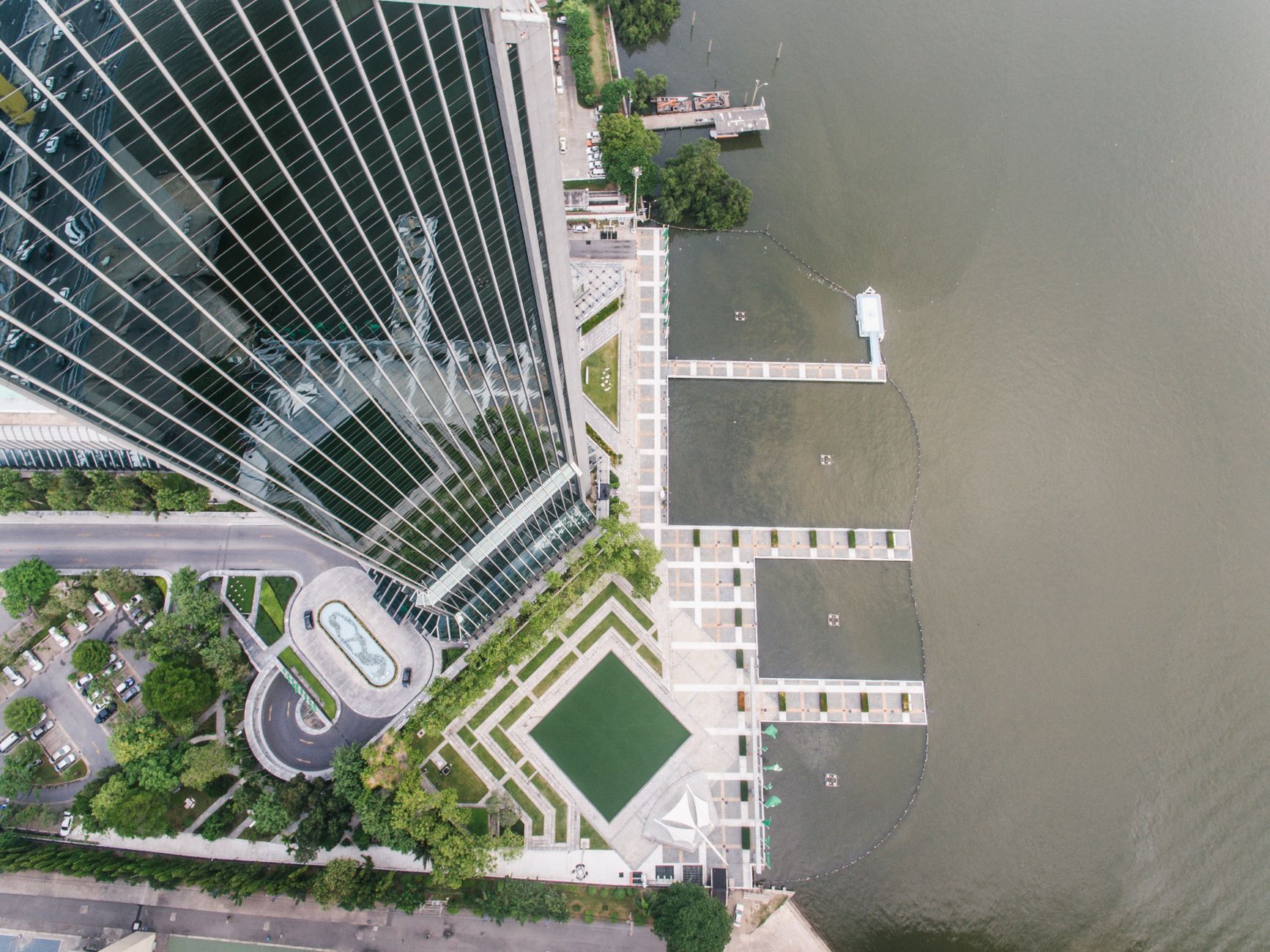 Aerial view of a modern skyscraper by a waterfront with geometric landscaping.