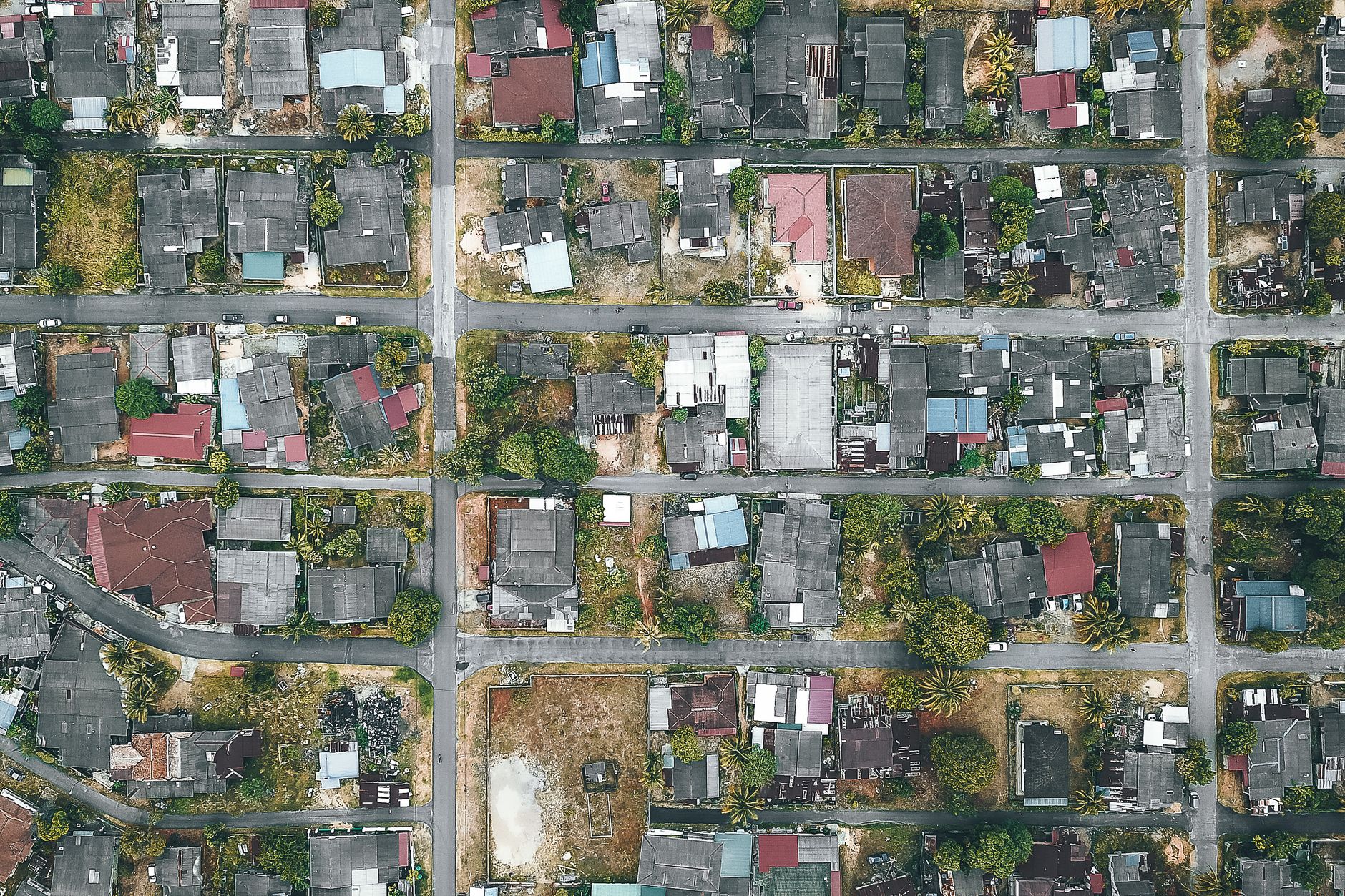 Overhead view of roadways and roofs of aged dwelling housing complexes near trees in suburb